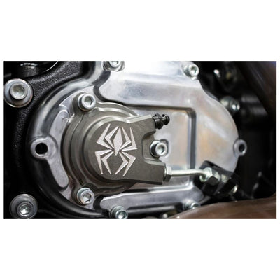 A hydraulic clutch slave cylinder from Rekluse, designed for Harley '17-'21 M8 Touring and '17-'21 Softail models, featuring a metallic automotive part with an engraved spider emblem, three bolt holes, and an asymmetric design to ensure reduced clutch lever pull.