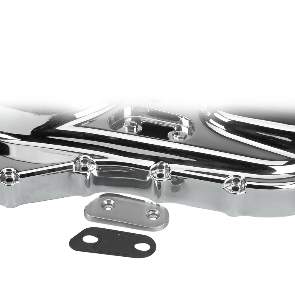 A close-up of a shiny metal engine or machine part, possibly from a Harley-Davidson Sportster, with two smaller metal and rubber gaskets—including a James Inspection Cover Gasket for 2004-2022 Harley-Davidson Sportster by James Gaskets—placed in front of it on a white background.