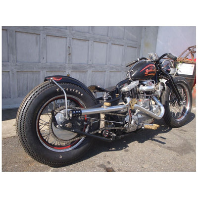 A motorcycle parked in front of a garage with a Monster Craftsman Weld On Chain Tensioner - Skate Wheel (Powell Peralta).