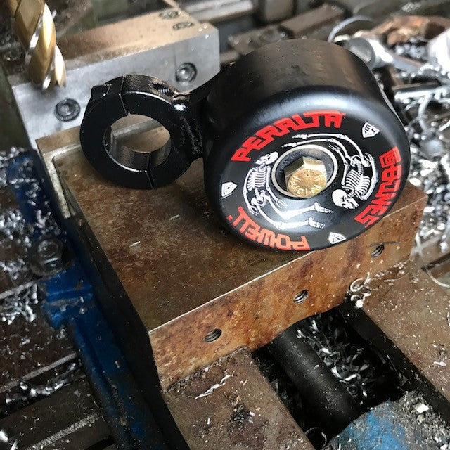 A heavy duty steel Clamp On Post Chain Tensioner - Skate Wheel (Powell Peralta)- 1.125" is sitting on a piece of metal.