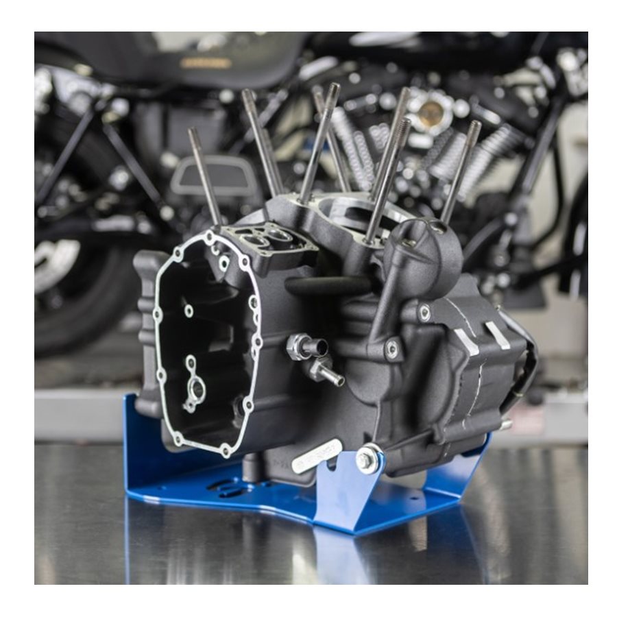 A product from S&S Cycle, the Engine Stand for Harley 2017+ M8 Motors, holds a Harley engine on a blue stand set on a metal surface, with another motorcycle blurred in the background.