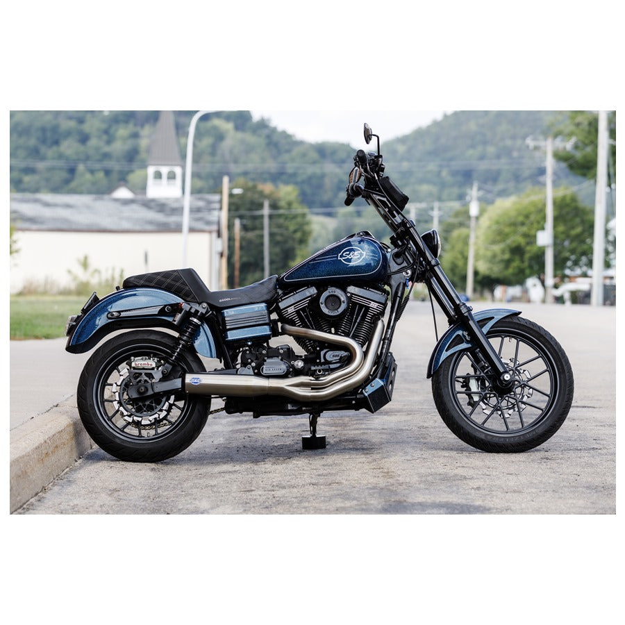 A motorcycle parked on the side of the road with a Brushed Stainless Qualifier 2 into 1 Exhaust System for 2006-2017 Harley Davidson Dyna Models designed by S&S Cycle.