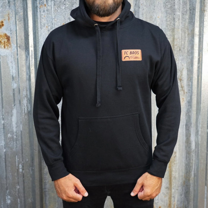 Badge Hoodie - Black/Orange, a classic streetwear piece, with a TC Bros logo embroidered on the left chest.