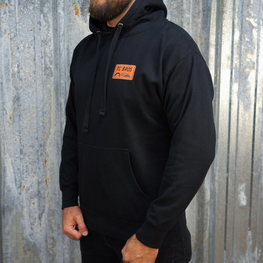 Badge Hoodie - Black/Orange, a classic streetwear piece, with a TC Bros logo embroidered on the left chest.