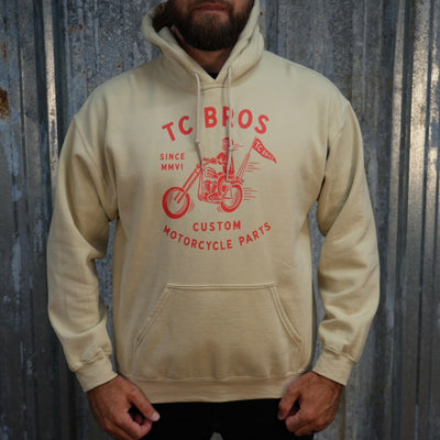 Beige Rider Hoodie - Sand featuring a red graphic of a motorcycle and text advertising TC Bros. custom motorcycle parts, printed on demand.