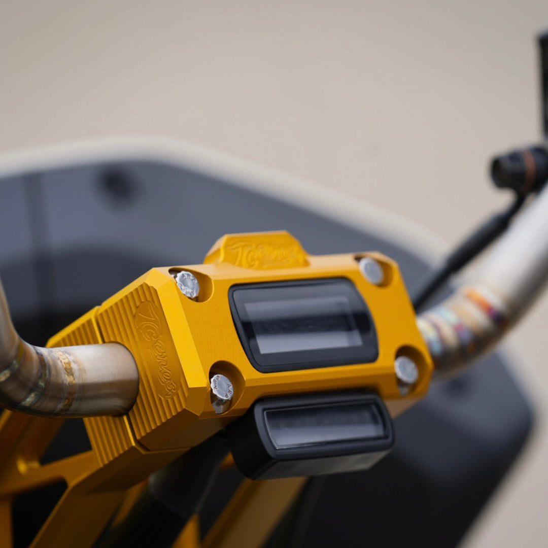 Close-up of a motorcycle's handlebars featuring yellow brackets and TC Bros. Pro Series Pullback Truss Riser for Harley M8 Softail Digital Gauge, highlighting American craftsmanship in the detailed control buttons and grips, with rear-view mirrors reflecting the paved surface below.