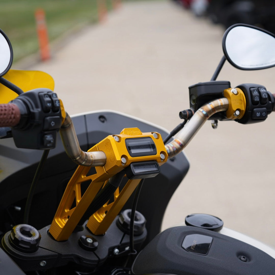 Close-up of a motorcycle's handlebars featuring yellow brackets and TC Bros. Pro Series Pullback Truss Riser for Harley M8 Softail Digital Gauge, highlighting American craftsmanship in the detailed control buttons and grips, with rear-view mirrors reflecting the paved surface below.