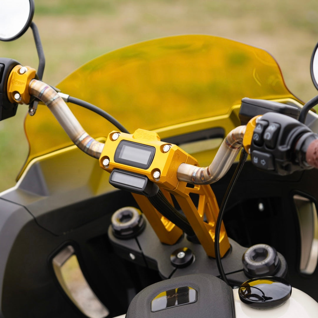 Close-up of a motorcycle's handlebars featuring yellow brackets and TC Bros. Pro Series Pullback Truss Riser for Harley M8 Softail Digital Gauge, highlighting American craftsmanship in the detailed control buttons and grips, with rear-view mirrors reflecting the paved surface below.