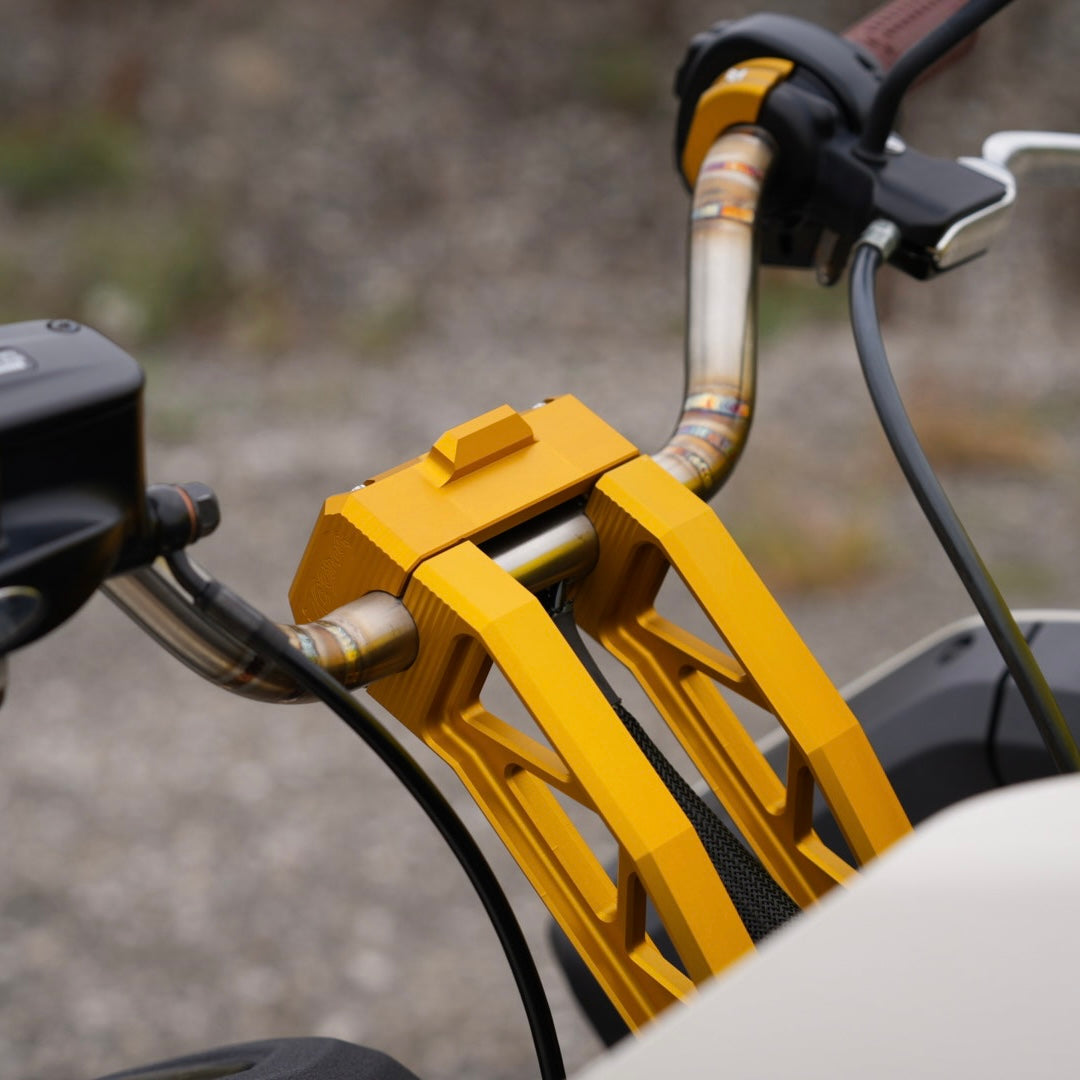 The TC Bros. Pro Series Pullback Truss Risers for Harley models by TC Bros. are CNC-machined, anodized metal handlebar risers available in gold, black, and silver. They feature a geometric design with visible bolts, perfect for Harley Davidson enthusiasts.