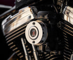 A close-up of a motorcycle engine showcases a Sportster points cover with a red and black emblem. Shiny chrome parts reflect light, highlighting Pangor Cycles' Cheap Sucker Bird Catcher/Air Cleaner for Harley-Davidson Carburetors, against a blurred background for sleek focus.