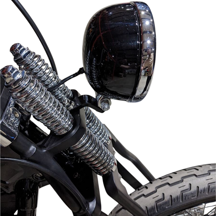 Two TC Bros. Springer Headlight Mounting Brackets with screws, washers, and nuts are shown on a white background. A partial view of a TC Bros. Springer Headlight Mounting Bracket and a motorcycle handlebar mirror appear in the lower right corner.