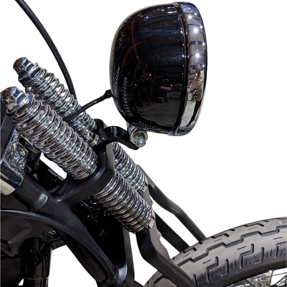 Two TC Bros. Springer Headlight Mounting Brackets with screws, washers, and nuts are shown on a white background. A partial view of a TC Bros. Springer Headlight Mounting Bracket and a motorcycle handlebar mirror appear in the lower right corner.