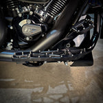 Close-up of TC Bros. Pro Series MX Slim Floorboards for 1984-Up Harley-Davidson Touring, featuring CNC-machined billet aluminum and visible bolts, mounted on a black Harley-Davidson motorcycle on a concrete floor.