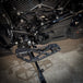 TC Bros. Pro Series MX Slim Floorboards for Harley Davidson Bagger Touring Models feature a skeletal design with metal pins, resembling high-performance pedals in silver, black, and gold. Arranged diagonally, they offer a striking visual appeal.