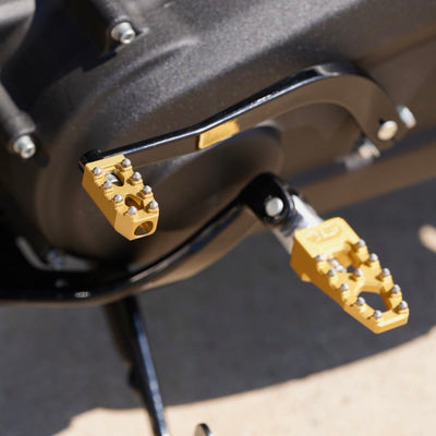 A close up of a motorcycle with TC Bros. Pro Series Gold MX Lite Rider Foot Pegs for 2018-newer Harley Softail & Pan America.