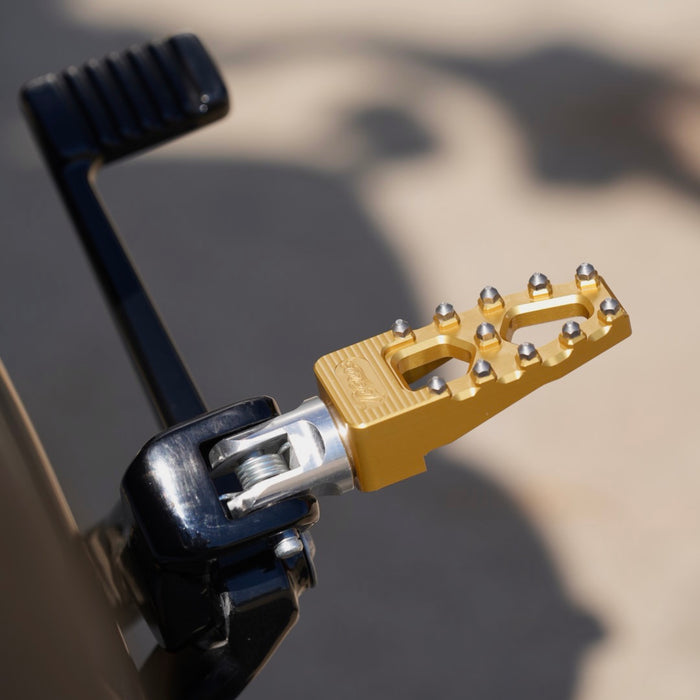 A close up of a TC Bros. motorcycle with TC Bros. Pro Series Gold MX Lite Rider Foot Pegs for 2018-newer Harley Softail & Pan America and a yellow brake pedal.