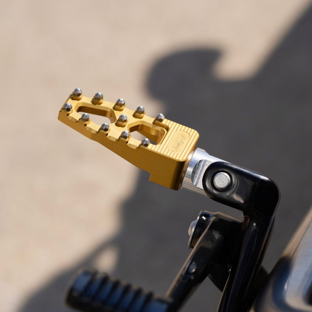 A close up of a motorcycle with TC Bros. Pro Series Gold MX Lite Rider Foot Pegs for 2018-newer Harley Softail & Pan America handlebar grip, providing high traction and stability.