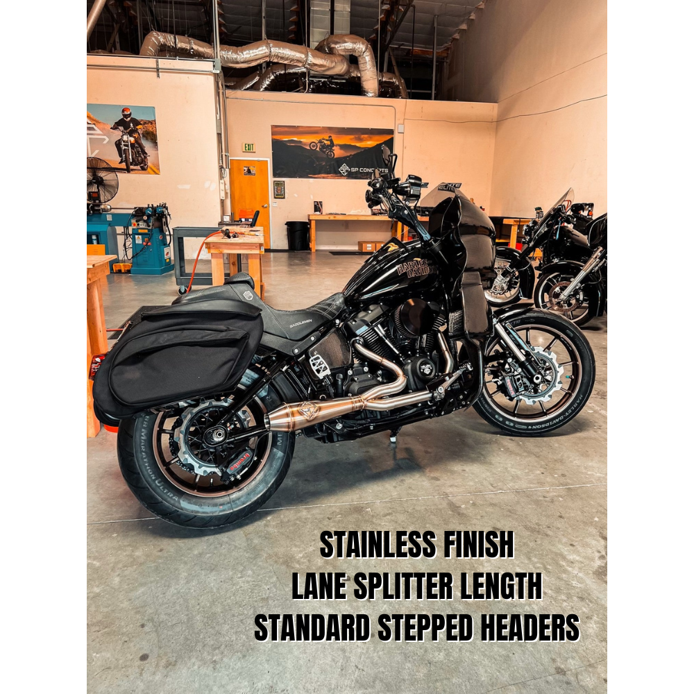 The SP Concepts Big Bore Exhaust for M8 Softail ST & Sport Glide (2018-Present) in stainless steel, featuring welded joints and a hexagonal logo emblem, rests on a metallic work surface, highlighting its premium finish.