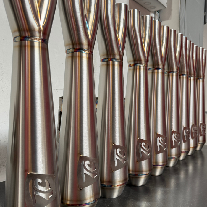 TC Bros. 2-into-1 Stainless Exhaust System for 2018-Up Harley-Davidson Softail by TC Bros., displayed with various Harley-Davidson Softail exhaust pipes in the background.