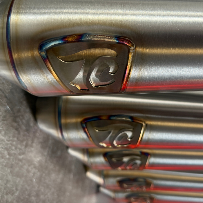 TC Bros. 2-into-1 Stainless Exhaust System for 2018-Up Harley-Davidson Softail by TC Bros., displayed with various Harley-Davidson Softail exhaust pipes in the background.