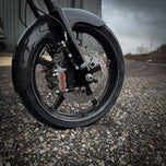 The TC Bros. Pro Series Radial Caliper Brake Line Kit for Harley Touring 2014-2023 includes silver and black bolts, washers, spacers, and two braided hoses with metal connectors, all arranged on a white background. Brand: TC Bros.