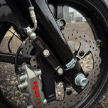 The TC Bros. Pro Series Radial Caliper Brake Line Kit for Harley Touring 2014-2023 includes silver and black bolts, washers, spacers, and two braided hoses with metal connectors, all arranged on a white background. Brand: TC Bros.