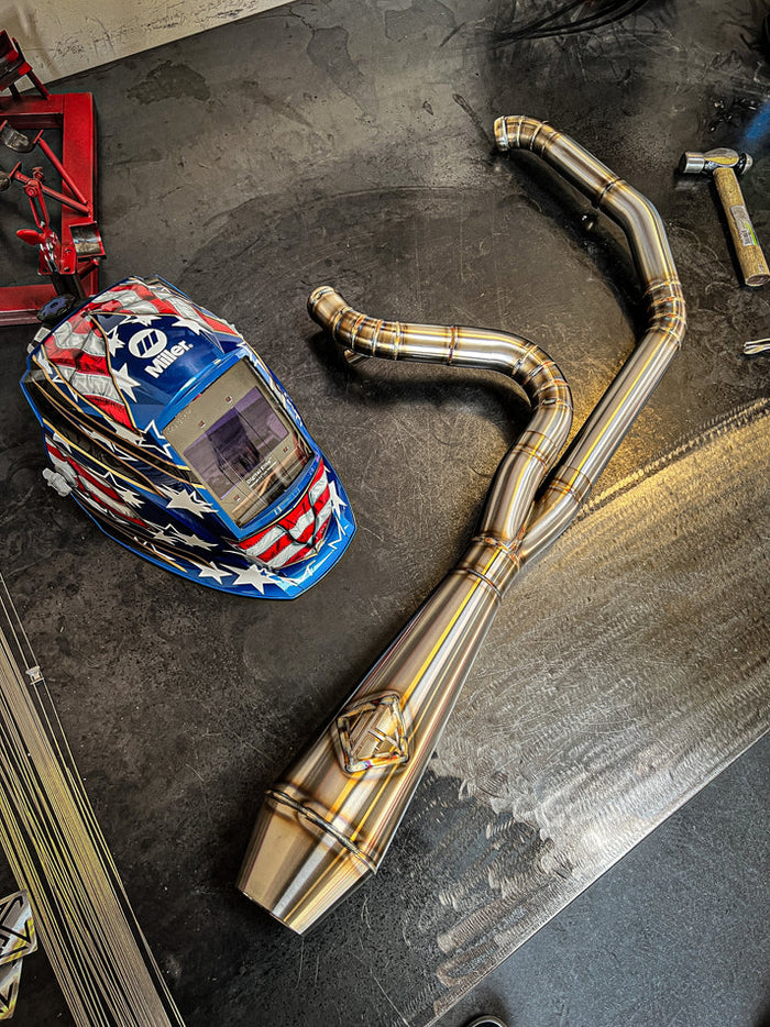 A motorcycle with a SP Concepts Works Edition Big Bore Exhaust M8 Touring FLT 2017-Present (stainless) helmet and Big Bore Exhaust pipes on a table.