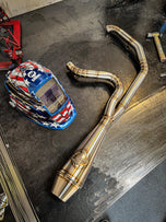 A motorcycle with a helmet and SP Concepts Works Edition Big Bore Exhaust Dyna 1999-2005 (Stainless) pipes on a table.
