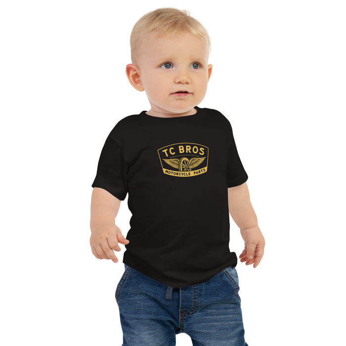 Toddler in a TC Bros. baby short sleeve tee with winged wheel logo and blue jeans standing against a white background.