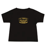 Toddler in a TC Bros. baby short sleeve tee with winged wheel logo and blue jeans standing against a white background.