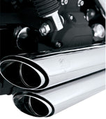 A silver and black cruiser-style motorcycle with chunky tires, a chrome Vance & Hines Short Shots Exhaust System for 06-09 Fat Bob, Dyna, Low, Wide & Super Glide, and a single seat, viewed from the rear left side.