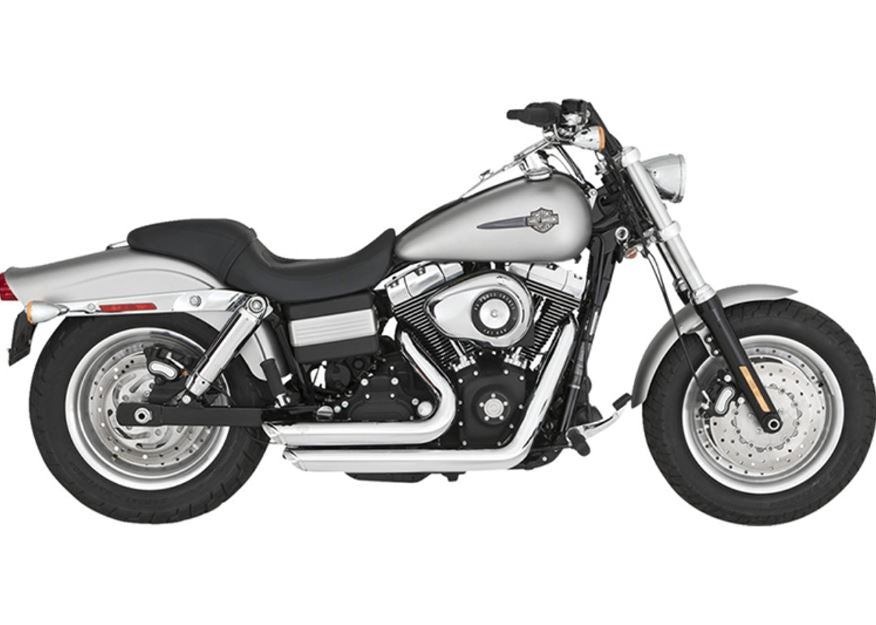 A silver and black cruiser-style motorcycle with chunky tires, a chrome Vance & Hines Short Shots Exhaust System for 06-09 Fat Bob, Dyna, Low, Wide & Super Glide, and a single seat, viewed from the rear left side.