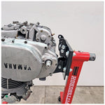 A Yamaha motorcycle engine is securely mounted on a Chop Source Deluxe Yamaha XS650 Engine Stand Brackets by Chop Source, positioned against a plain white wall.