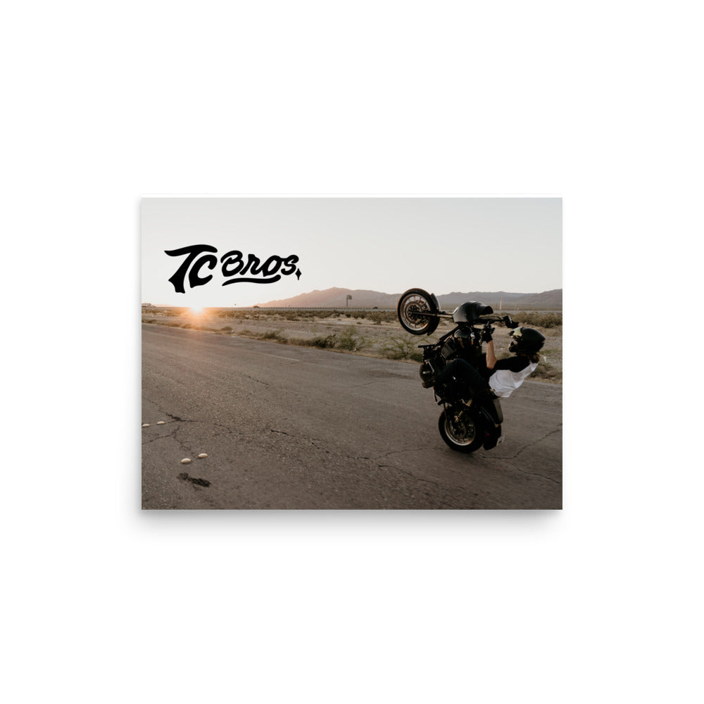 TC Bros. Dyna Wheelie Poster performing a wheelie at sunset on an empty road, captured vividly on matte paper.