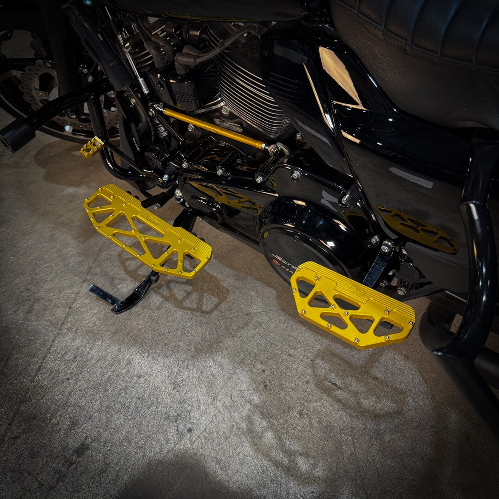 Close-up of a Harley-Davidson Bagger’s left side, featuring black bodywork, engine, and TC Bros. Pro Series MX Passenger Floorboards for 1993-Up Touring models with yellow metal accents on a concrete floor.