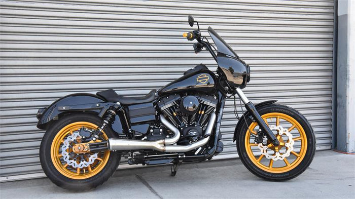 A black motorcycle with gold accents, featuring a windshield, large exhaust pipe, and spoke wheels fitted with a Bassani The Ripper Road Rage 2-into-1 Stainless Exhaust 06-17 FXD (w/Mids), 07-17 FXD/FXDWG (w/Forwards).