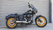 A black motorcycle with gold accents, featuring a windshield, large exhaust pipe, and spoke wheels fitted with a Bassani The Ripper Road Rage 2-into-1 Stainless Exhaust 06-17 FXD (w/Mids), 07-17 FXD/FXDWG (w/Forwards).