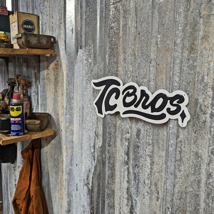 A TC Bros. Metal Shop Sign - Stamped Aluminum with the word "icons" in a cursive font, affixed to a textured gray stamped aluminum surface.