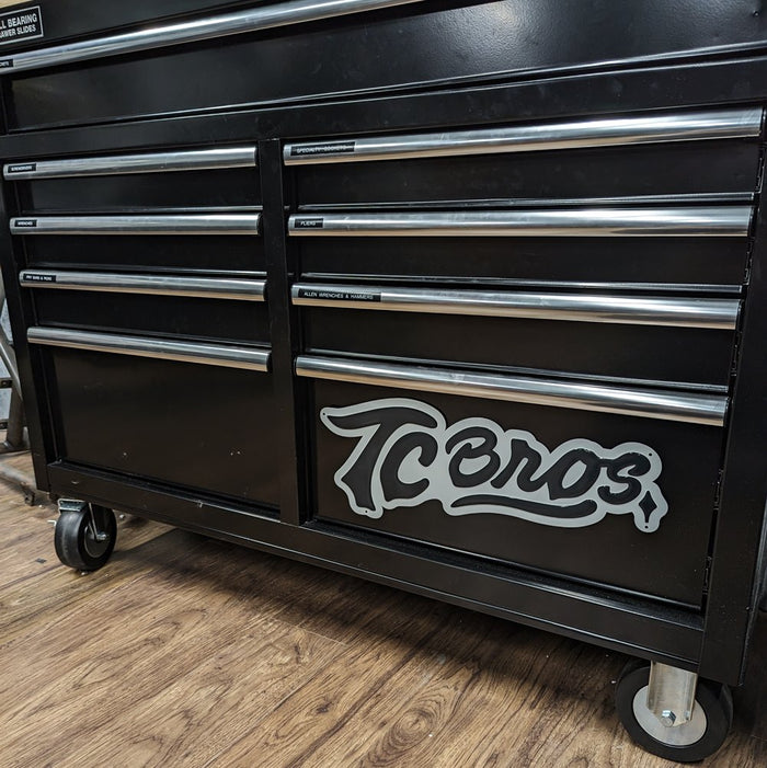 A TC Bros. Metal Shop Sign - Stamped Aluminum with the word "icons" in a cursive font, affixed to a textured gray stamped aluminum surface.