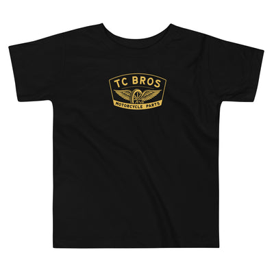 Toddler wearing a TC Bros. Winged Wheel Black/Gold cotton t-shirt, paired with jeans.