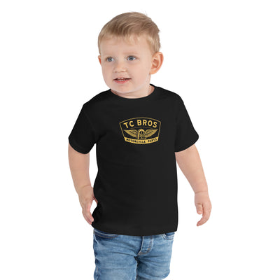 Toddler wearing a TC Bros. Winged Wheel Black/Gold cotton t-shirt, paired with jeans.