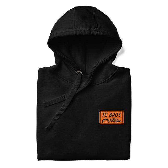 Badge Hoodie - Black/Orange, a classic streetwear piece, with a TC Bros logo embroidered on the left chest.