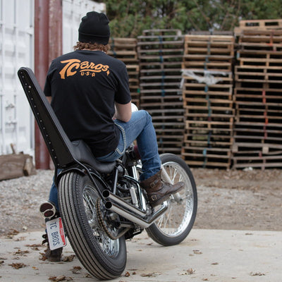 A man sitting on a TC Bros. Classic T-Shirt - Black, by TC Bros motorcycle.
