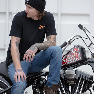 A man with tattoos sitting on a TC Bros. Classic T-Shirt - Black motorcycle.