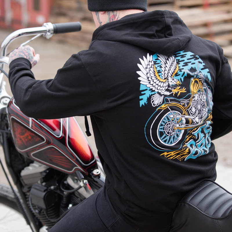 A man on a motorcycle wearing a black TC Bros. Eagle Zip Hoodie - Black with an eagle on it.