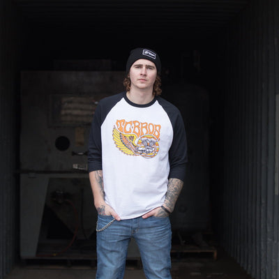 A young man wearing a TC Bros. Wing Raglan - White/Black t-shirt, pre-shrunk., standing in a warehouse.