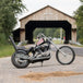A black TC Bros. chopper motorcycle parked in front of a covered bridge, with TC Bros. 1" Rabbit Ears Handlebars - Black Smooth.