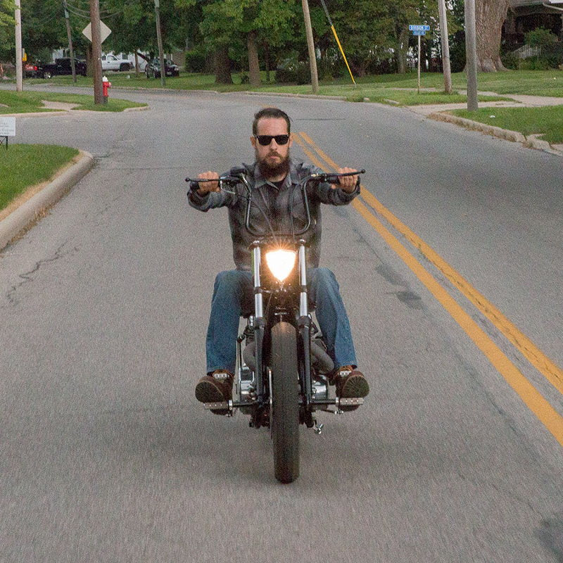 A man riding a motorcycle down a street, gripping TC Bros.' 7/8" Lane Splitter™ Handlebars - 9.25" Rise Black Powdercoat.
