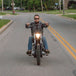 A man riding a motorcycle down a street, gripping TC Bros.&