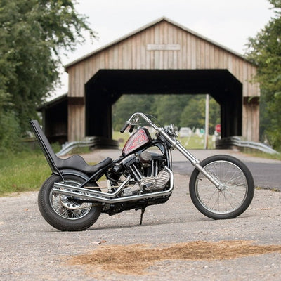 A TC Bros. motorcycle with chrome accents parked in front of a covered bridge.